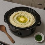 Slow cooker full of creamy mashed potatoes with melting butter and chives